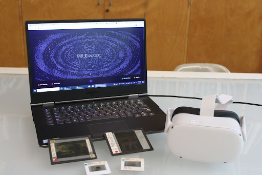 An arrangement of tools utilized by the UNH CAT Lab such as glass slides, and a virtual reality headset alongside a computer accessing Midjourney 